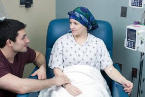 una donna in un letto di ospedale sta affrontanto la chemioterapia con il supporto del proprio compagno a fianco