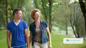 Un uomo e una donna camminano nel verde di un parco mano nella mano